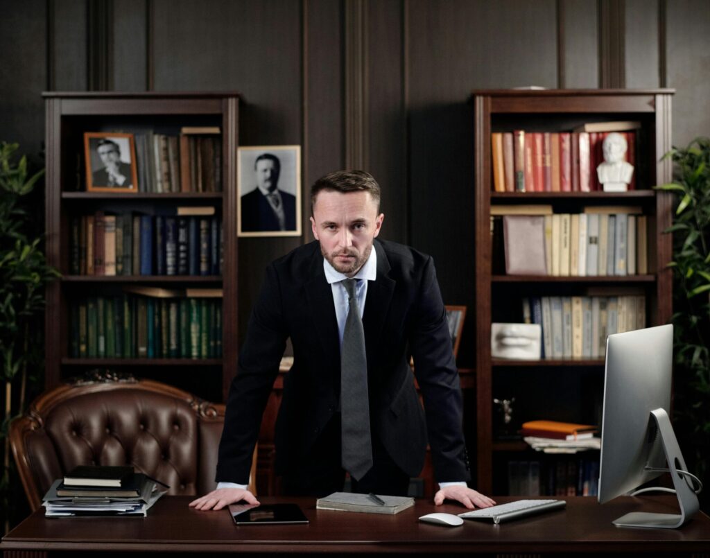 Confident businessman standing at desk with USA flag in office library.